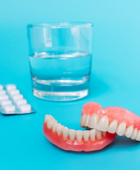 Dentures, glass of water, and cleaning solution tablets on a blue background