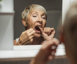 Woman flossing her teeth in bathroom mirror