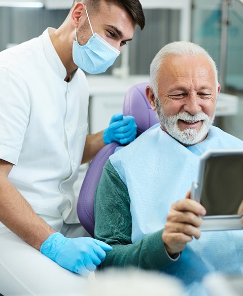 Man with dentures in Fayetteville smiling in dentist's mirror