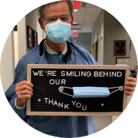 Fayetteville dentist holding a sign reading we're smiling behind our facemasks thank you