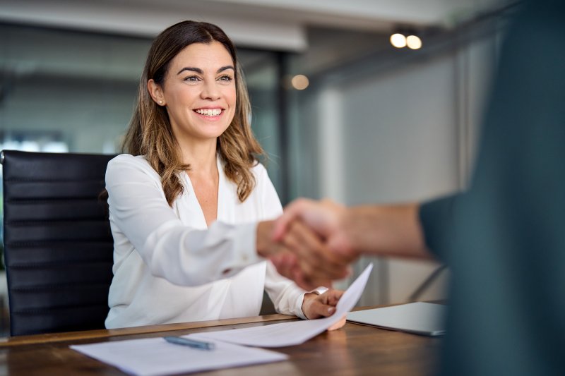 A woman who just had cosmetic dentistry done shaking hands with a client