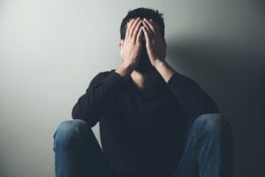 Sad man sitting with hands covering face.